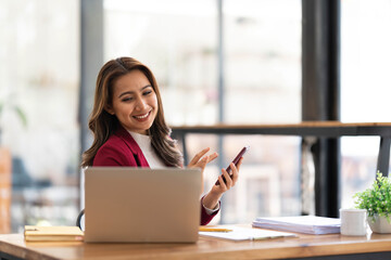 Obraz premium Smiling beautiful Asian businesswoman analyzing chart and graph showing changes on the market and holding smartphone at office.