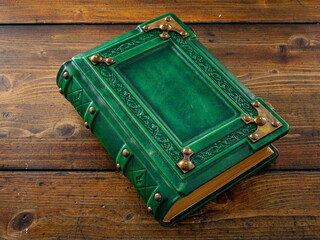 Vintage, medieval green leather book with embossed frame and metal corners lay down to wooden table 
