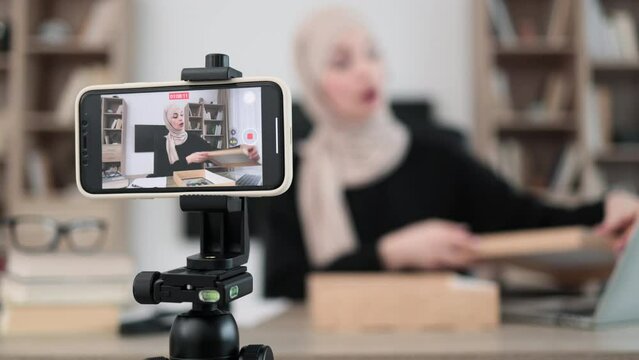 Focus on phone screen , muslim woman recording video on phone camera while unpacking box with new wireless tablet. Female influencer sharing with subscribers her positive feedback about new order.