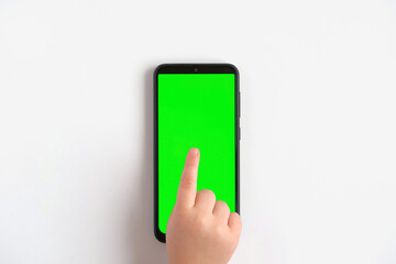 Child hand touching clicking on mobile phone with chromakey screen. Little Baby Finger Taps in the center of blank phone green display. Close up 4K Footage. Using smartphone device. Top view Flat lay