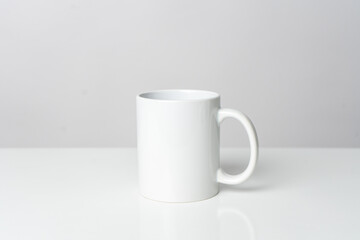 A white blank coffee mug on the top of a white table with a white background