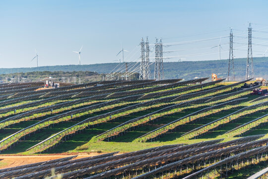Aerial. Station's solar panels cover the fields of Portuguese hills to generate clean, ecological electrical energy. High voltage poles in background.