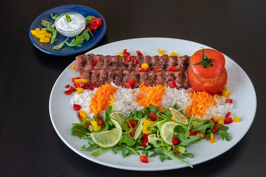 Lula kebab from veal chicken with rice, vegetables and sauce on a black background.