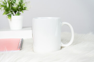 Fototapeta na wymiar A white blank coffee mug on the top of a white table decorated with minimalistic looks