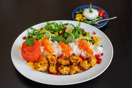 Jooje kebab from veal chicken with rice, vegetables and sauce on a black background.