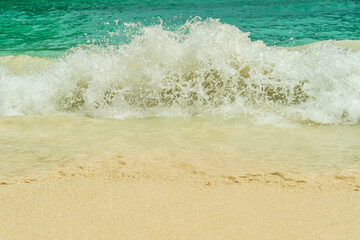 Turquoise sea waves crashing on the sandy beach spread beyond the foam.