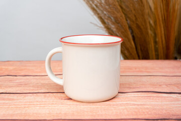A white blank enamel mug on the top of a wooden texture mat with minimalistic looks