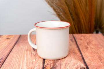 A white blank enamel mug on the top of a wooden texture mat with minimalistic looks