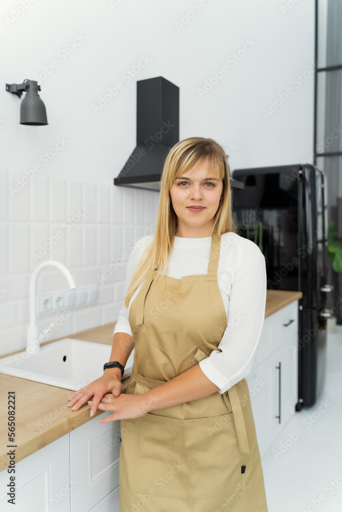 Wall mural smiling girl in an apron with her hands on the table and stands in the kitchen kitchen interior. the