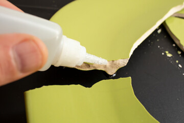 Hand applying liquid glue on ceramic broken pieces, repairing a green plate - obrazy, fototapety, plakaty