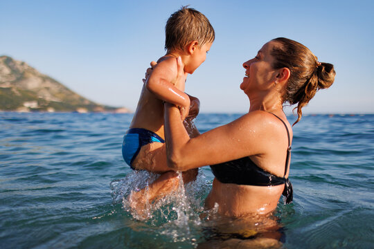 Cheerful mother plays with her son in the sea
