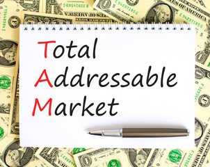 TAM total addressable market symbol. Concept words TAM total addressable market on white note on a beautiful background from dollar bills. Business TAM total addressable market concept. Copy space.
