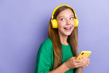 Photo of cheerful adorable lady use hold iphone earbuds gadget look interested empty space offer isolated on purple color background - obrazy, fototapety, plakaty