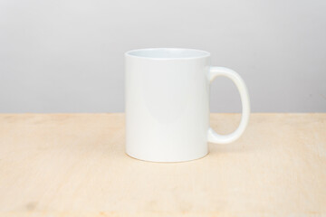 A white blank coffee mug on the top of a plywood with a clean white background behind it