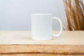 A white blank coffee mug on the top of a plywood with some simple rustic flower at the background