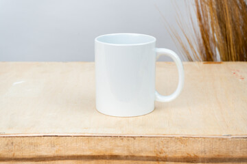 A white blank coffee mug on the top of a plywood with some simple rustic flower at the background