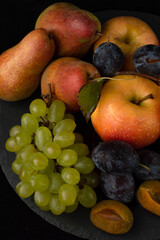 Blurred image of a still life with grapes, apples, pears and plums on a dark background.