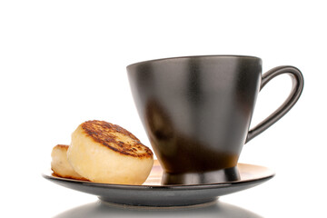 Two homemade cheese pancakes on a black ceramic saucer with a black cup, macro, isolated on white background.
