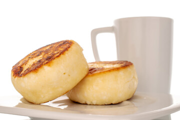 Two homemade cheese pancakes on a white ceramic saucer with a white cup, macro, isolated on a white background.