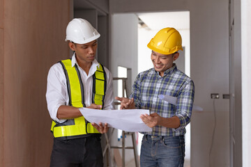 Two Asian male engineers are inspecting a job site and looking at drawings, consulting and debugging works to achieve quality work.