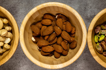 Wooden bowl with roasted almonds on a slate table. Top view, series photo with other dried fruits.