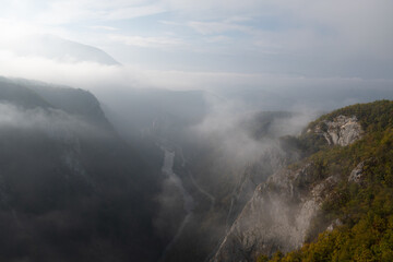 Mountain viewpoint over river canyon obscured in fog and clouds during autumn morning, misty mountain landscape
