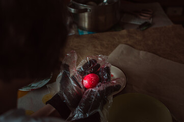 Girl in plastic gloves paints red Easter egg
