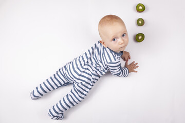 Portrait of happy little kid in striped clothes eating kiwi on white background. Healthy nutrition for kids.