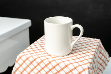A white blank coffee mug on the top of a hand cloth isolated with black color as the background