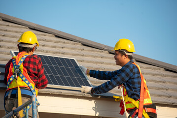 Young technician standing on metal platform installing heavy solar photo voltaic panel on blue sky background. Stand-alone solar panel system installation, efficiency and professionalism concept.