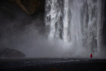 Fearless strong woman faces powerful waterfall; concept of strong and invincible woman, female strength, dangerous waterfall in iceland