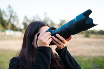 Young unrecognizable amateur photographer woman taking pictures to the sky with a telephoto lens.