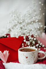 Happy valentines day! Cute stylish cup of tea with heart on cozy modern armchair with gifts, red envelope and white flowers. Valentine morning surprise for beloved