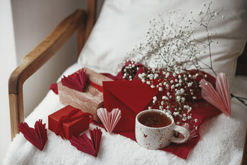 Happy valentines day! Cute stylish cup of tea with heart on cozy modern armchair with gifts, red...