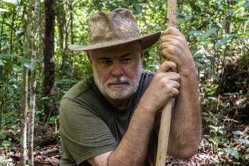 Middle-aged man walks aided by a wooden staff through the Atlantic forest. Apparently tired but...