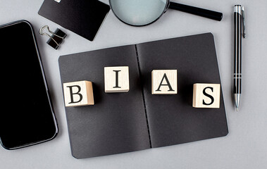 Word BIAS on wooden block on black notebook with smartpone, credit card and magnifier