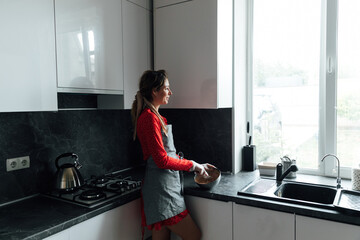 a woman cook in an apron prepares food and looks out the window