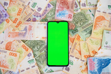 Mobile phone with green display on lots of currency notes of Argentine peso...