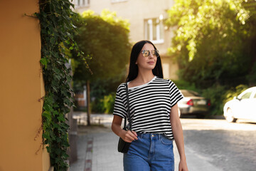 Fototapeta premium Beautiful young woman in stylish sunglasses walking on city street