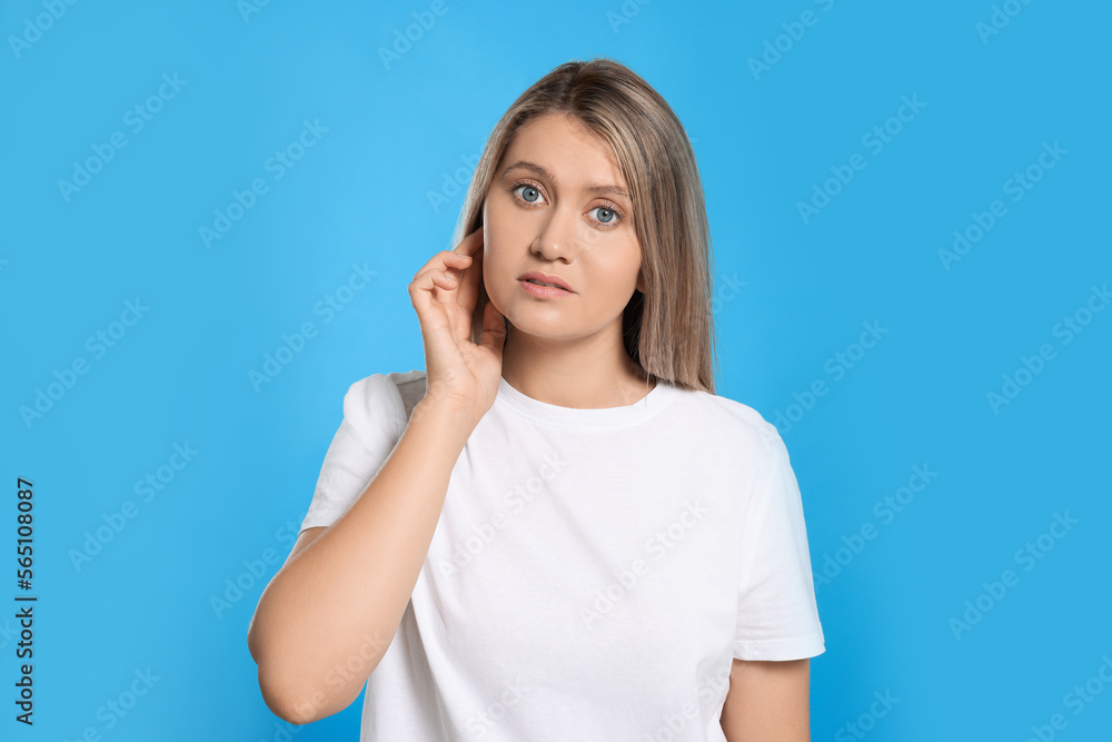 Sticker Young woman suffering from ear pain on light blue background