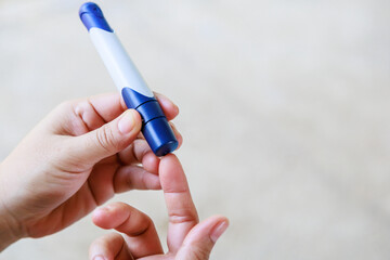 Close up of woman hands using lancet on finger to check blood sugar level by Glucose meter using as Medicine, diabetes, glycemia, health care and people concept.