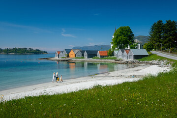 Two individuals stroll along a pristine white beach beside colorful waterfront houses under clear...