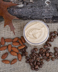  Natural handmade coffee and almond body butter with coffee beans and almond oil on beige and wooden background. Coffee and almond face cream, natural skin care.    