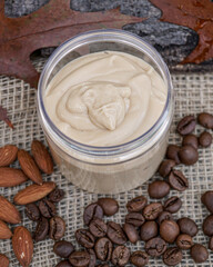  Natural handmade coffee and almond body butter with coffee beans and almond oil on beige and wooden background. Coffee and almond face cream, natural skin care.    