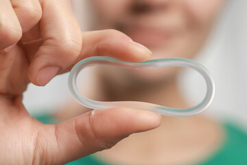 Fototapeta premium Woman holding diaphragm vaginal contraceptive ring on blurred background, closeup