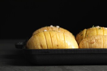 Raw Hasselback potatoes in baking pan on dark grey table, closeup