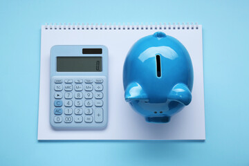 Piggy bank, notebook and calculator on light blue background, top view