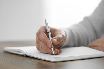 Man writing in notebook at wooden table indoors, closeup