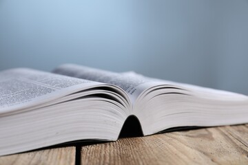 Closeup view of open Bible on wooden table against grey background. Religious book
