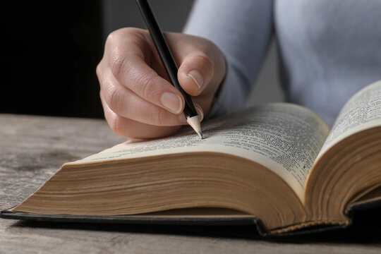 Woman marking up in Bible at wooden table, closeup